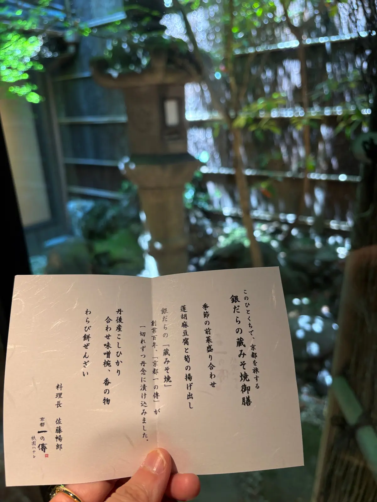 手で持つ日本語のカード、背景は緑の植物と木が並ぶ屋内空間