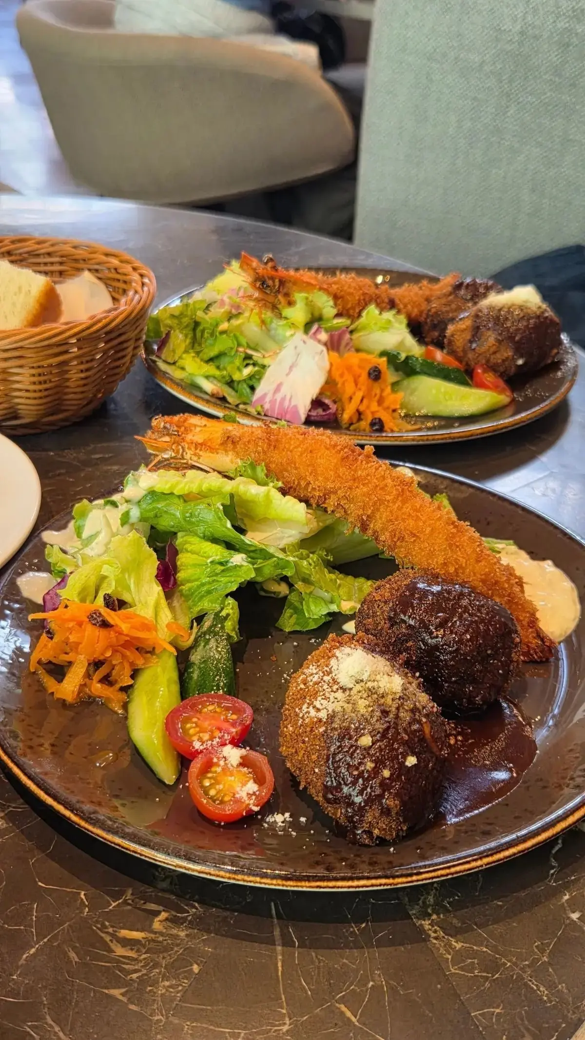 茶色のプレートにエビのフライ、トマト、きゅうり、にんじん、ラベルのサラダが盛り付けられ、ワゴンにパンが置かれている