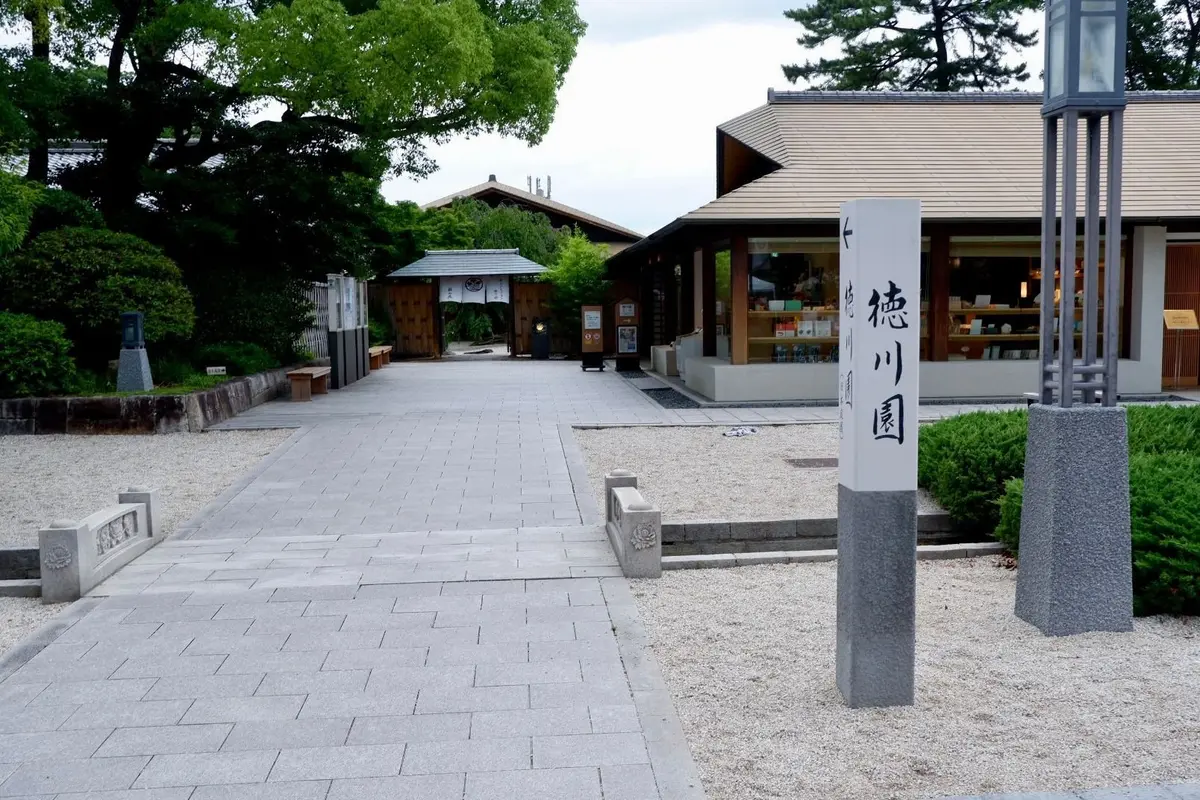 石造りの道が広がる徳川園の入り口、左右に木造の建物と緑の木々が並ぶ