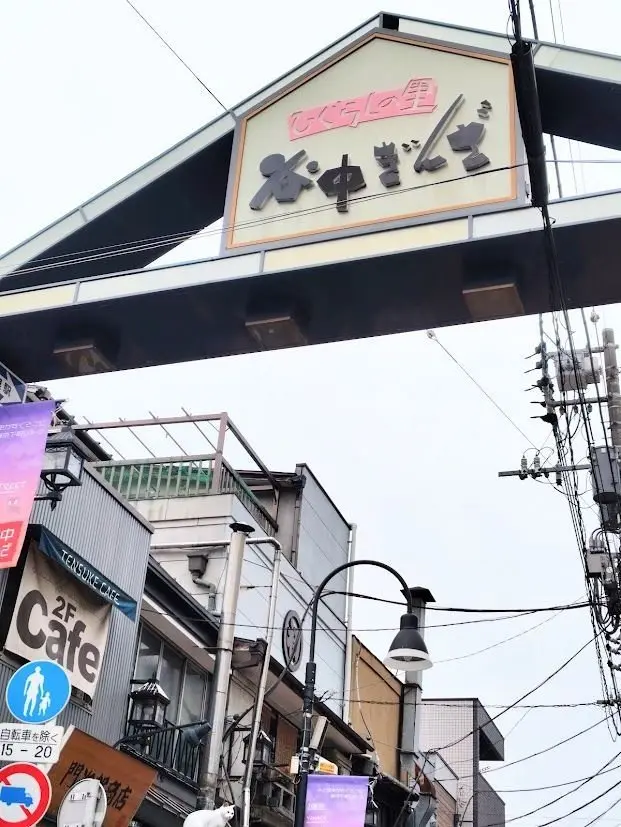 **「お好み焼き」の看板が設置された都市部の通りの様子** 

看板の上部には「お好み焼き」の文字がピンクと黒で表示され、下部には「松本」の文字が黒で書かれている。看板はガラスの屋根付きで、建物の上部に設置されている。