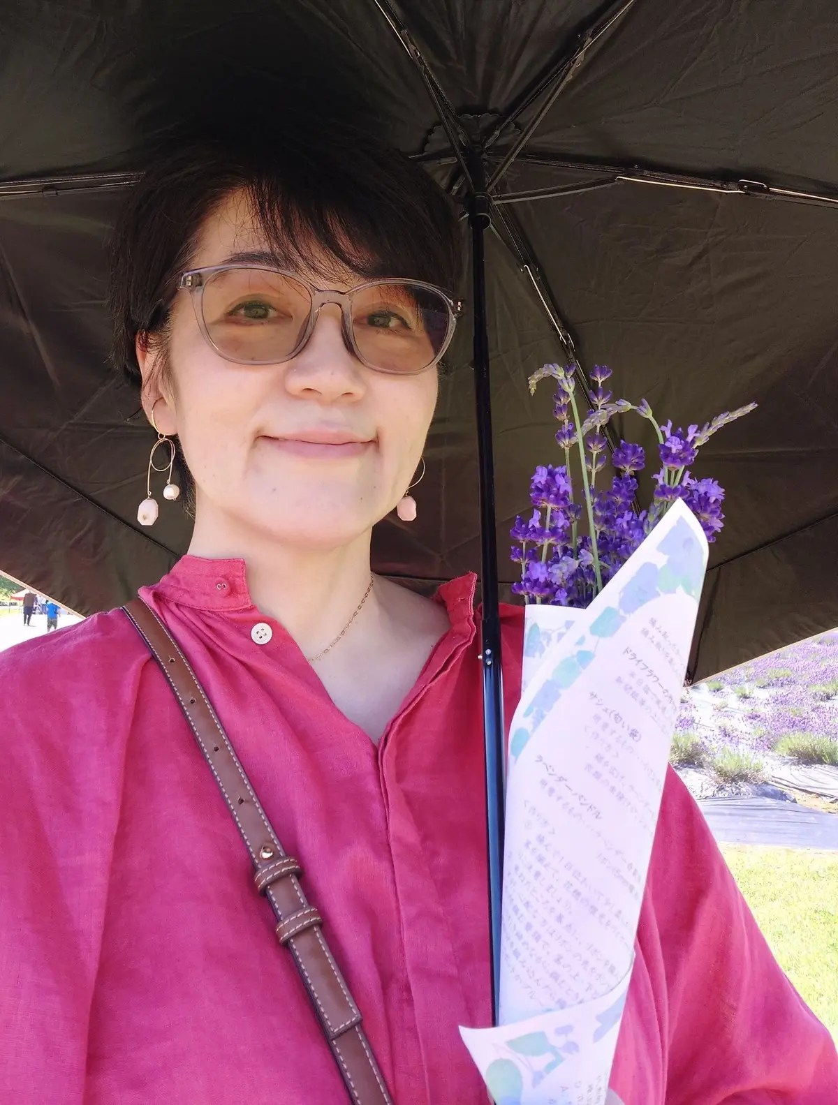 ピンクの服を着た女性が、紫の花を手に持って晴れた日に傘を差しています。