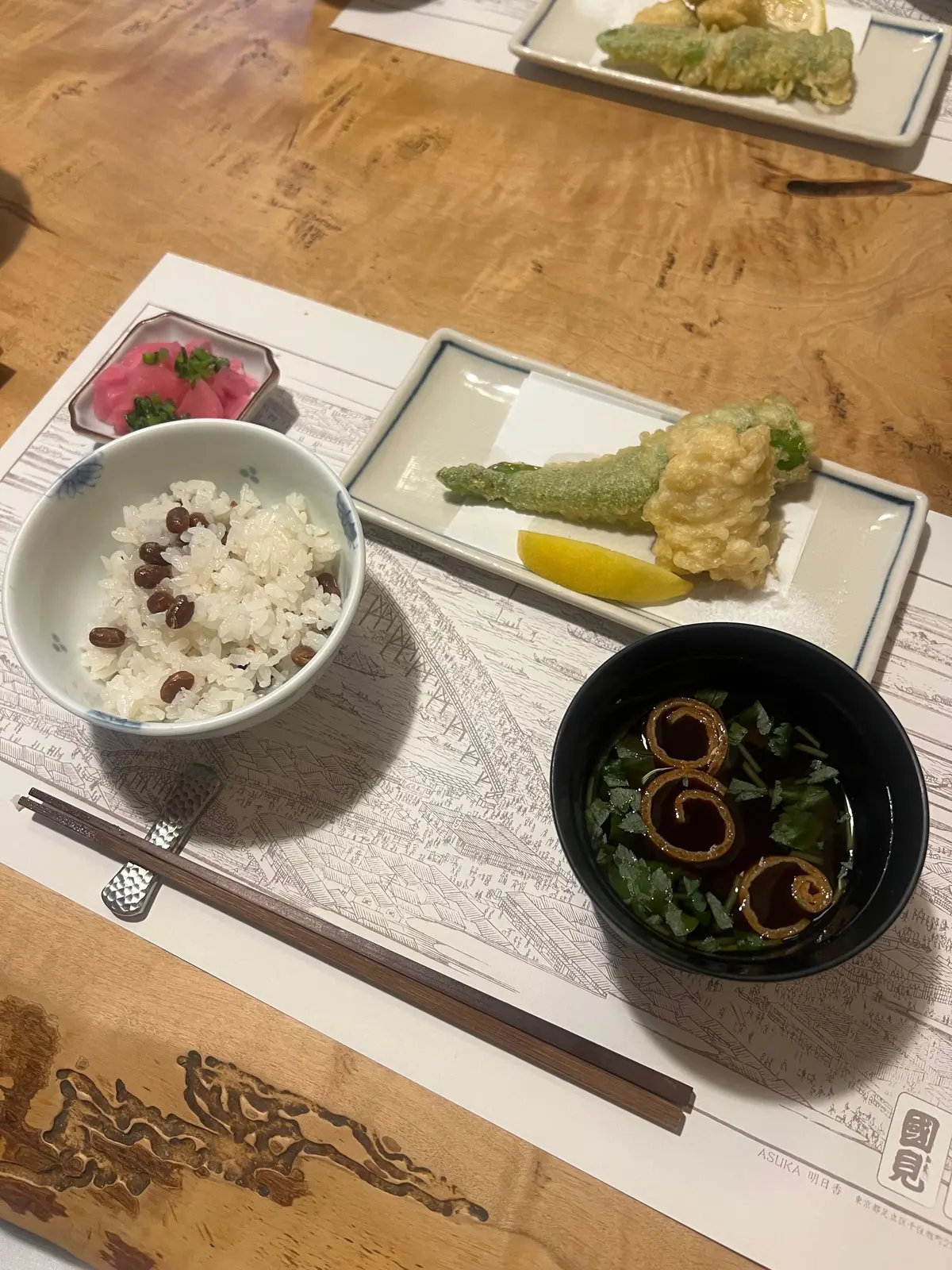 木のテーブルに白米と豆、天ぷら、わさび、ピクルス、ワサビ入りのお刺身が並んだ料理一式