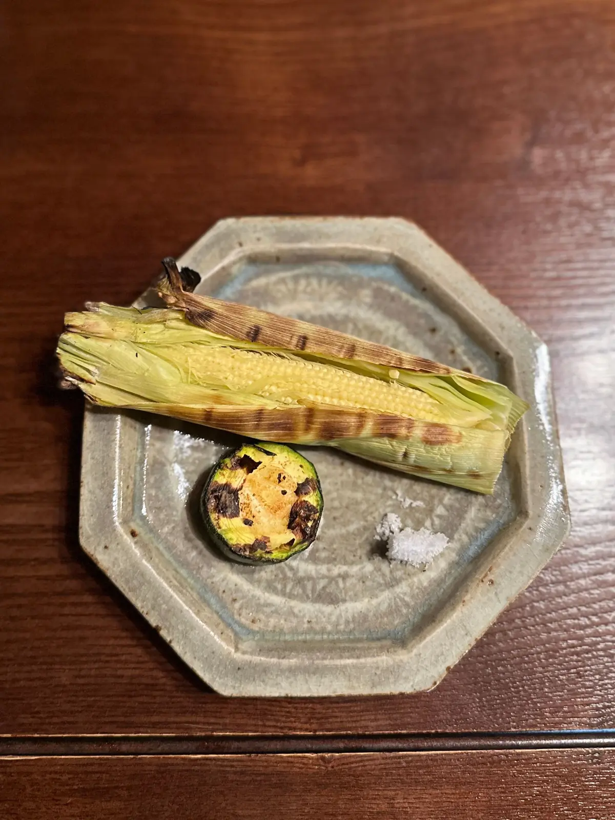 八角形の陶器皿に、グリルされたとうもろこし2本と、丸いカットされたとうもろこしが乗っている。粗塩が添えられている。