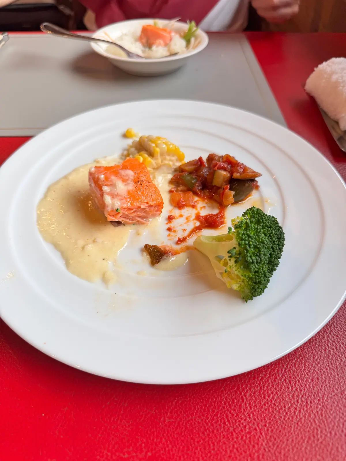 テーブルに置かれた白ワインのグラス、皿の料理、カトラリー。手前には白米と魚料理、奥にはサラダと他の料理が並ぶ。赤と白のテーブルクロスが目立つ。