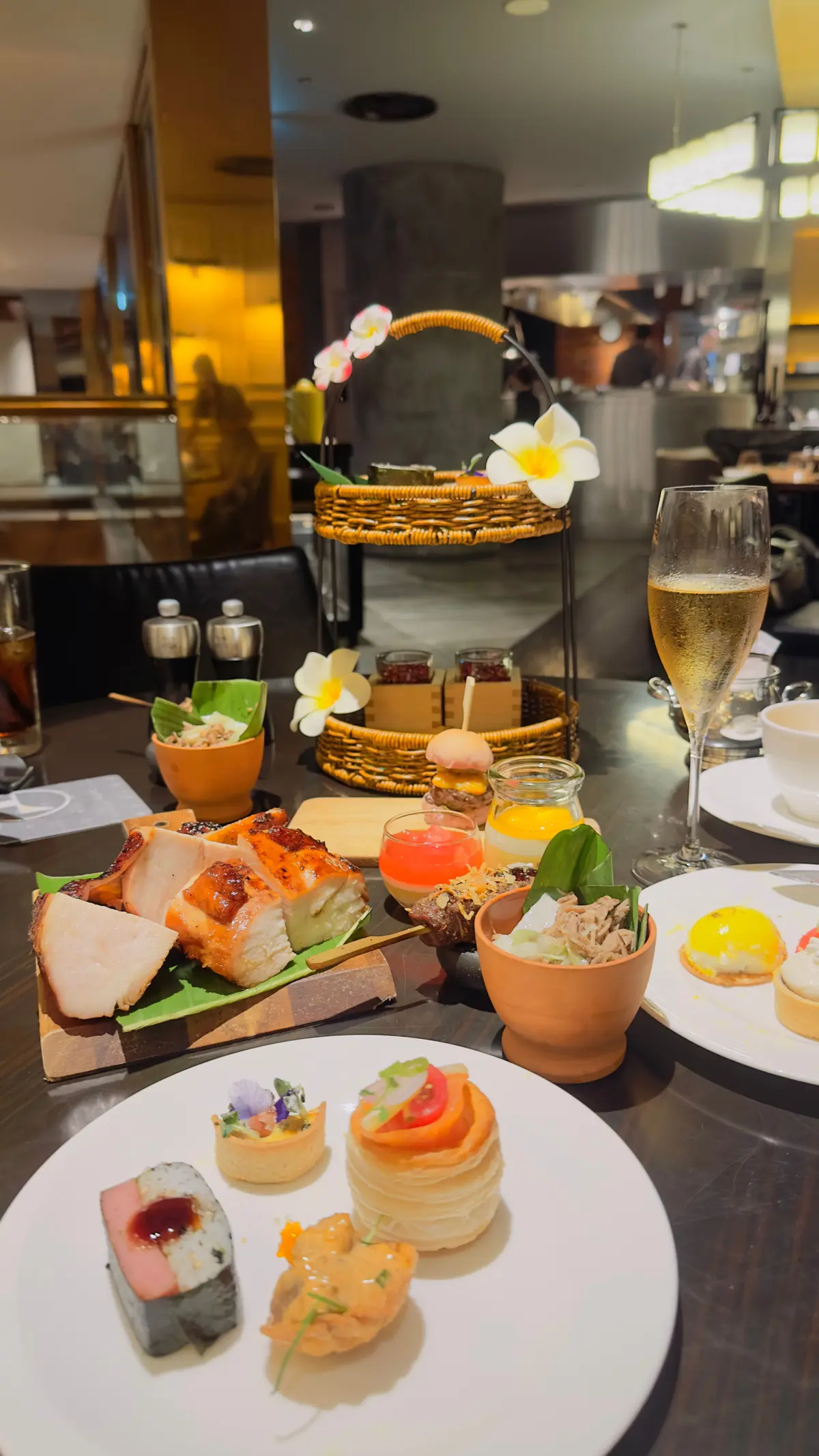 ワゴンの上に花が飾られたテーブルに、寿司、サンドイッチ、サラダ、ジュース、シャンパンなどが並ぶ料理が並んでいる。