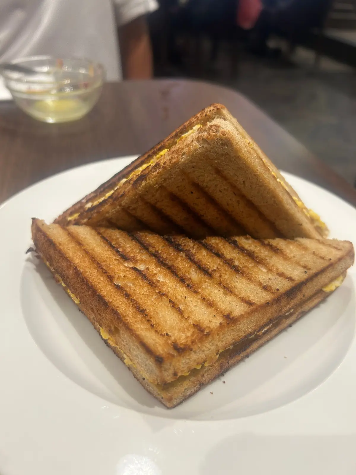 白い皿に、焼き目がついた三角形のチーズトーストが2つ重ねて置かれている。横には小さなガラスの器に入った液体がある。