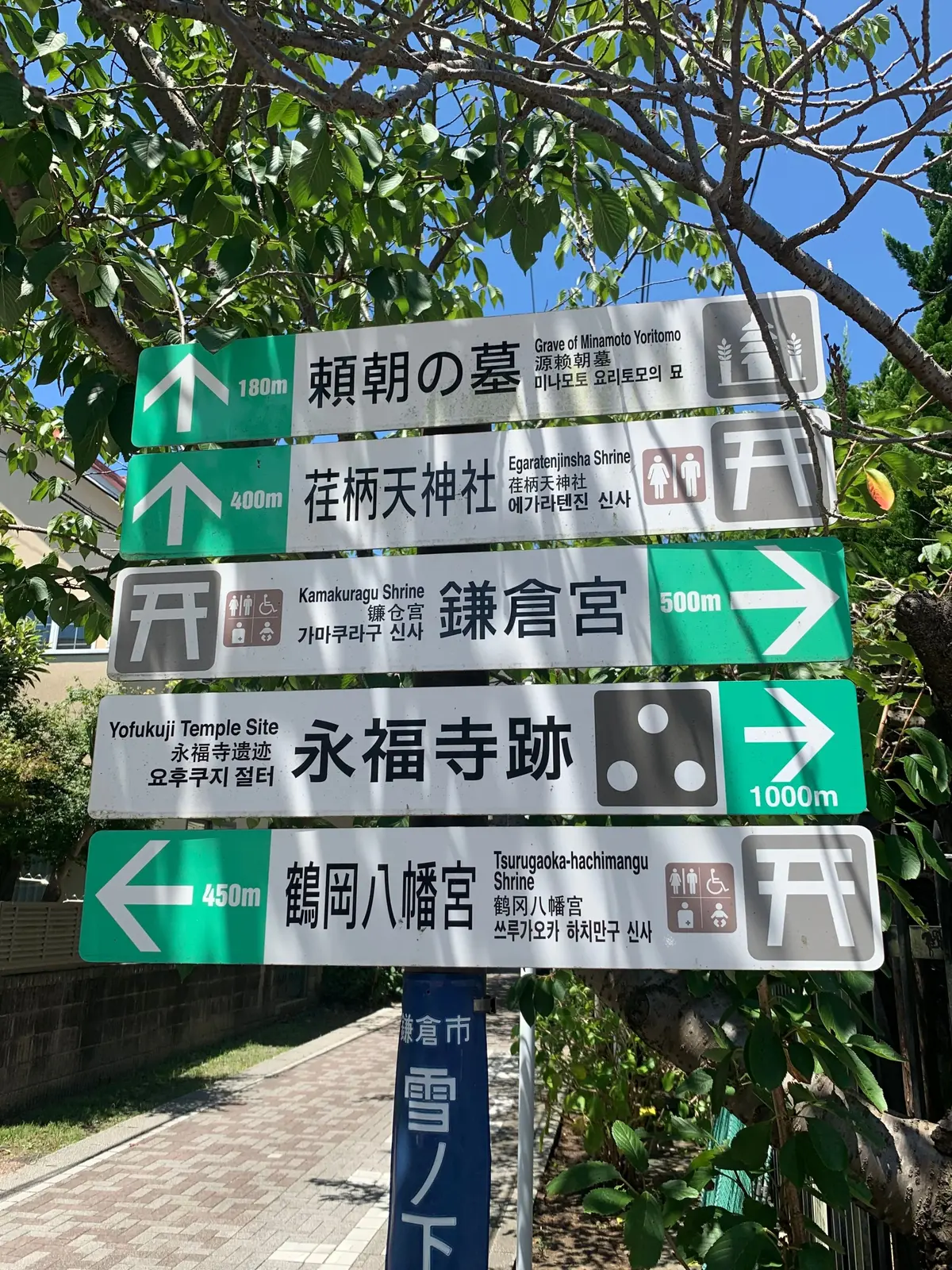 鎌倉市内の交差点に設置された、複数の方向指示標識。日本語、英語、韓国語で地名や施設名が記載され、距離も示されている。緑、青、黄色の帯で区切られ、上から順に「頼朝の墓」「荏柄天神社」「鎌倉宮」「永福寺跡」「鶴岡八幡宮」への案内。