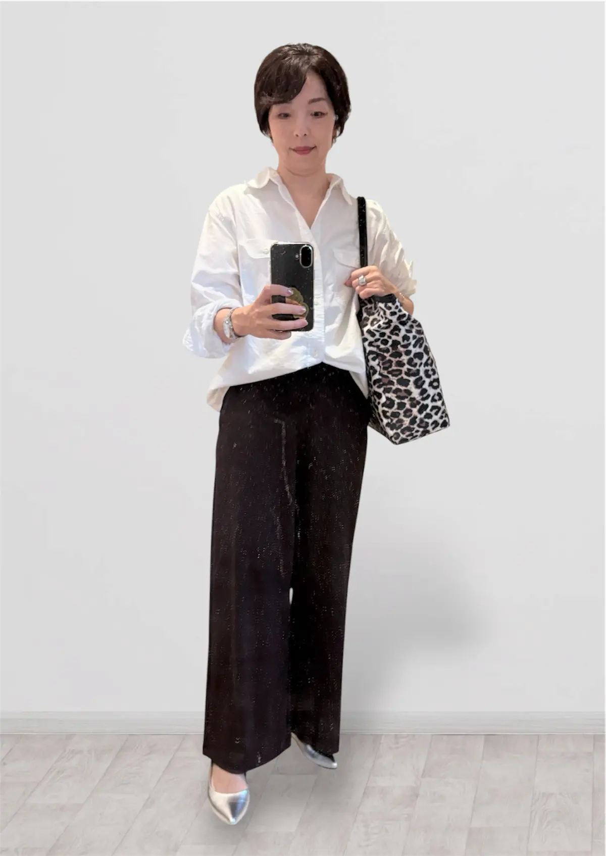 白いブラウスと黒いズボンを着た女性が、携帯電話を手に持って自撮り。レオパード柄のショルダーバッグを肩にかけており、銀色のハイヒールを履いている。