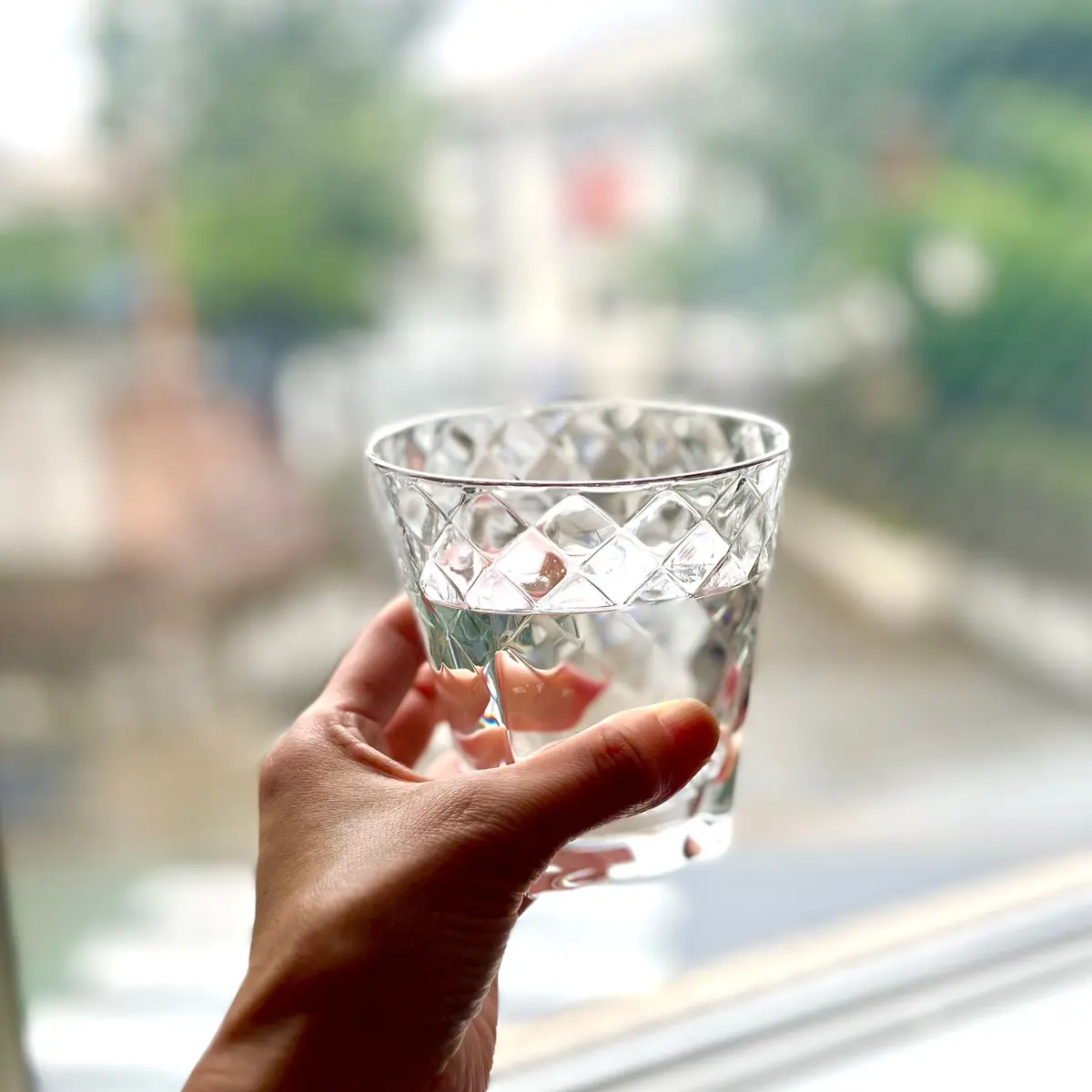 ガラス製の四角いカップを水で満たし、窓のそばで手で持っている。