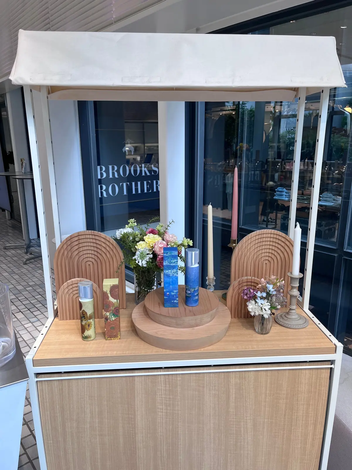 Brooks Brothersの店舗前にある、木製の台の上に置かれた装飾品。左右にアーチ型の木製オブジェ、中央には花瓶に入った花、キャンドルなどが配置されている。