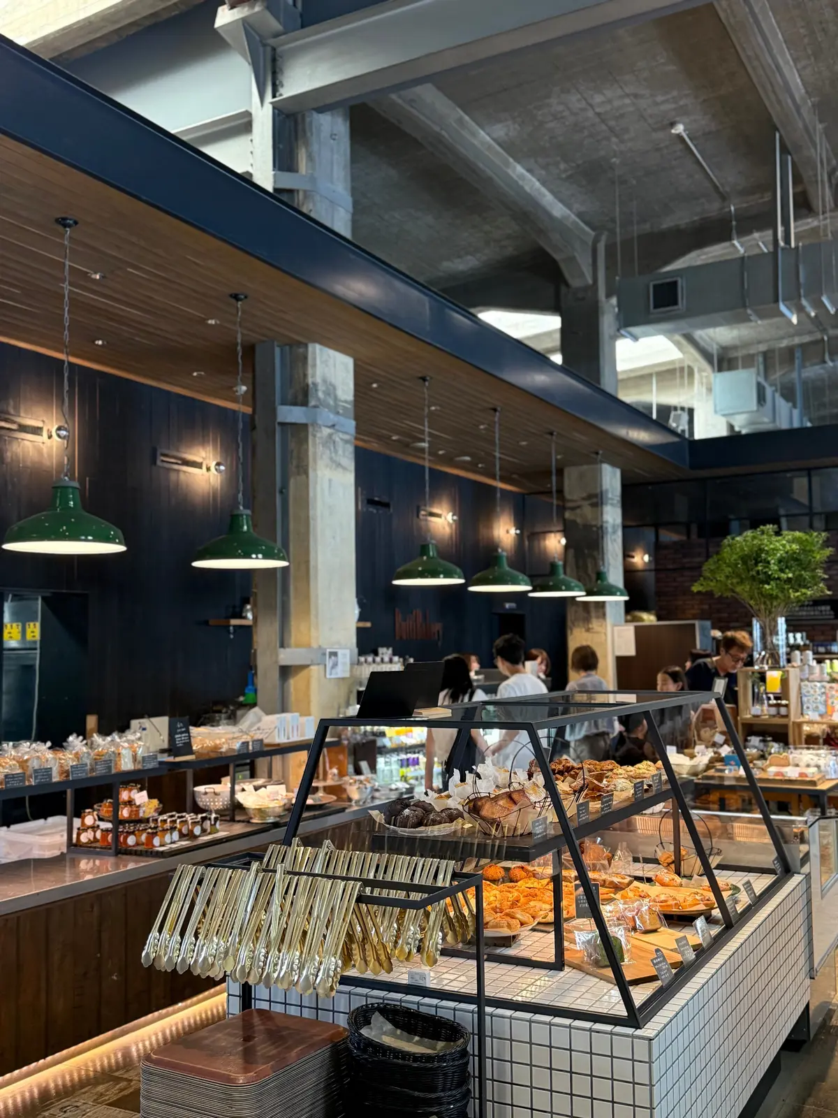 ペトリュスベーカリーの店内の様子。ショーケースにパンやペイストリーが並び、緑色のペンダントライトが吊り下げられている。木目調のカウンターと白いタイルが特徴的。