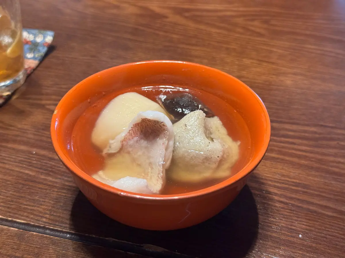 オレンジ色の器に、もちのような白い食材と黒い食材が甘い液体に浮かんでいる。