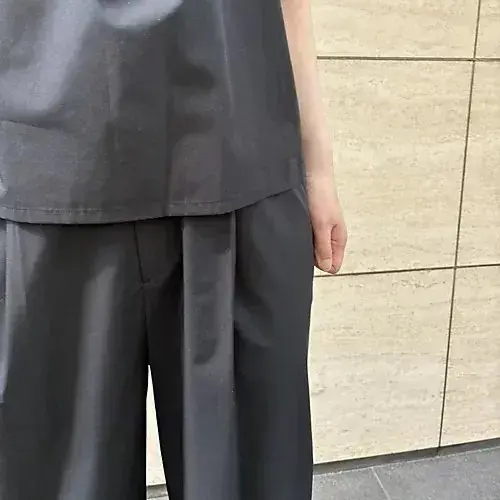 グレーのトップスとワイドパンツを着た人の後ろ姿、ベージュのタイル壁が背景にある