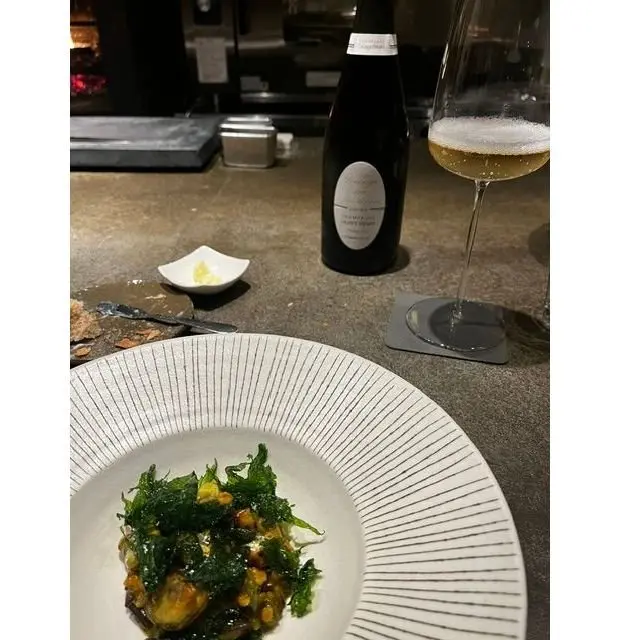 白いリネンプレートに盛り付けられた野菜とキノコのサラダ、ワイングラスと黒いボトルが置かれたカウンター