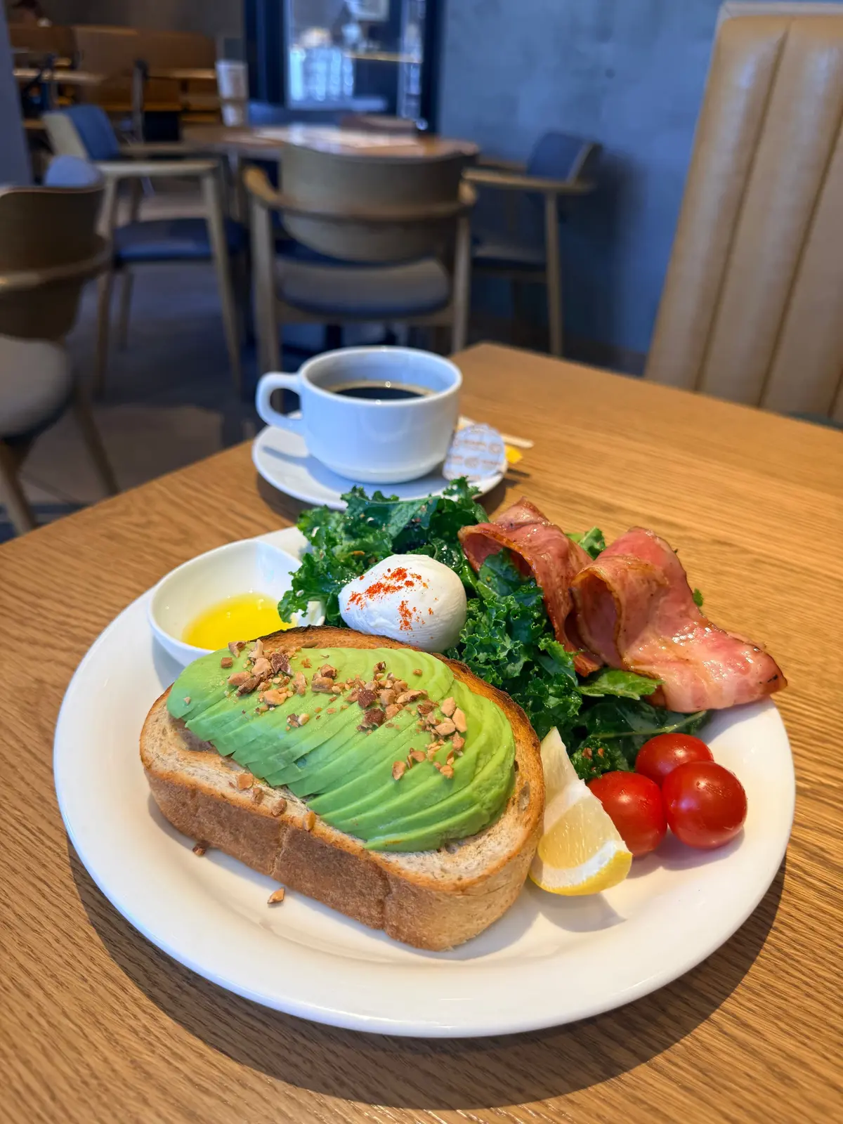 アボカドとトースト、ケールサラダ、トマト、ベーコン、卵黄がのった朝食プレートとコーヒー