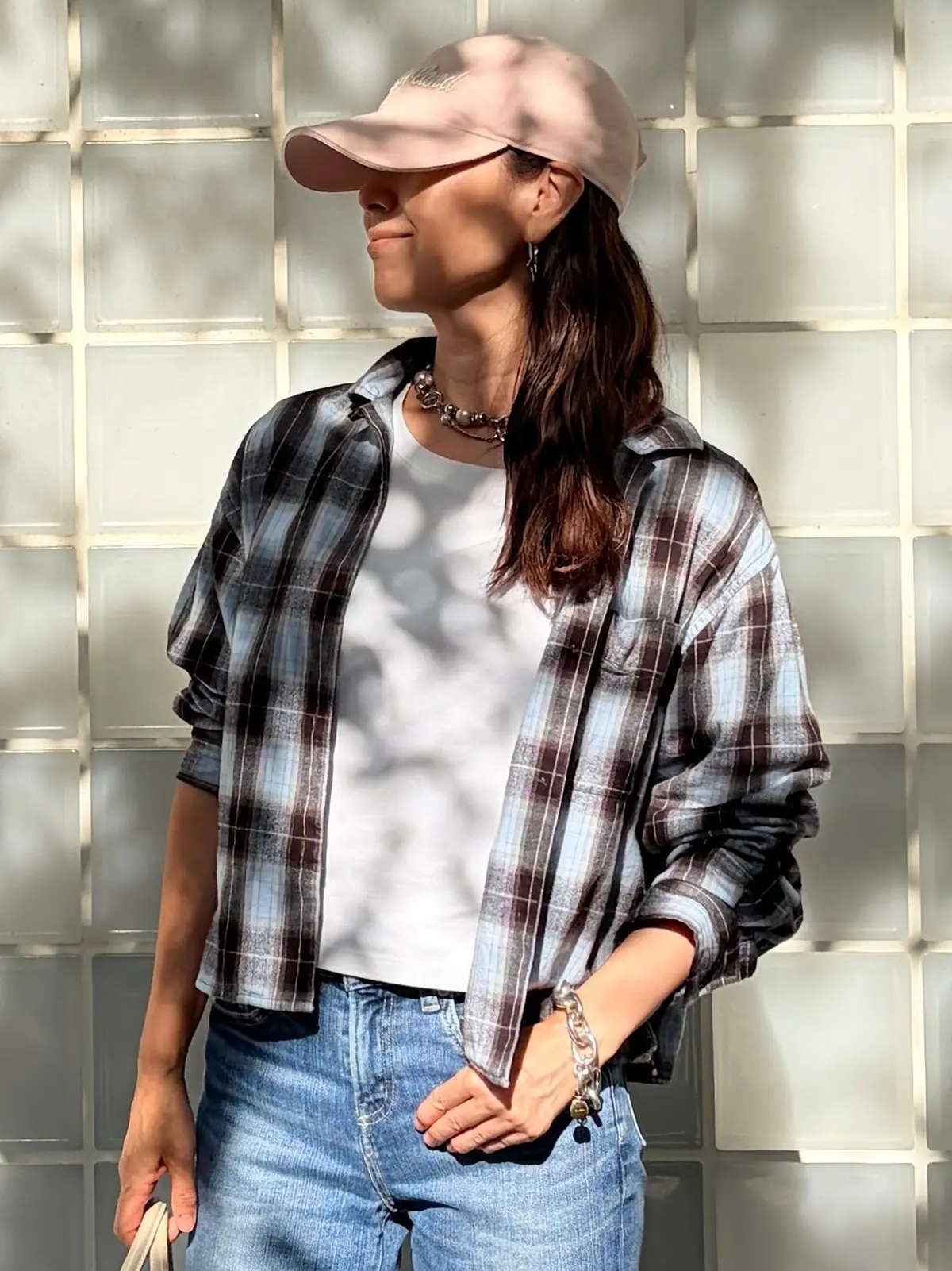 ベージュのキャップを被った女性が、白いTシャツに淡い青と茶色のチェック柄のシャツ、青いジーンズを着用。片手はポケットにINし、横を向いているポートレート。