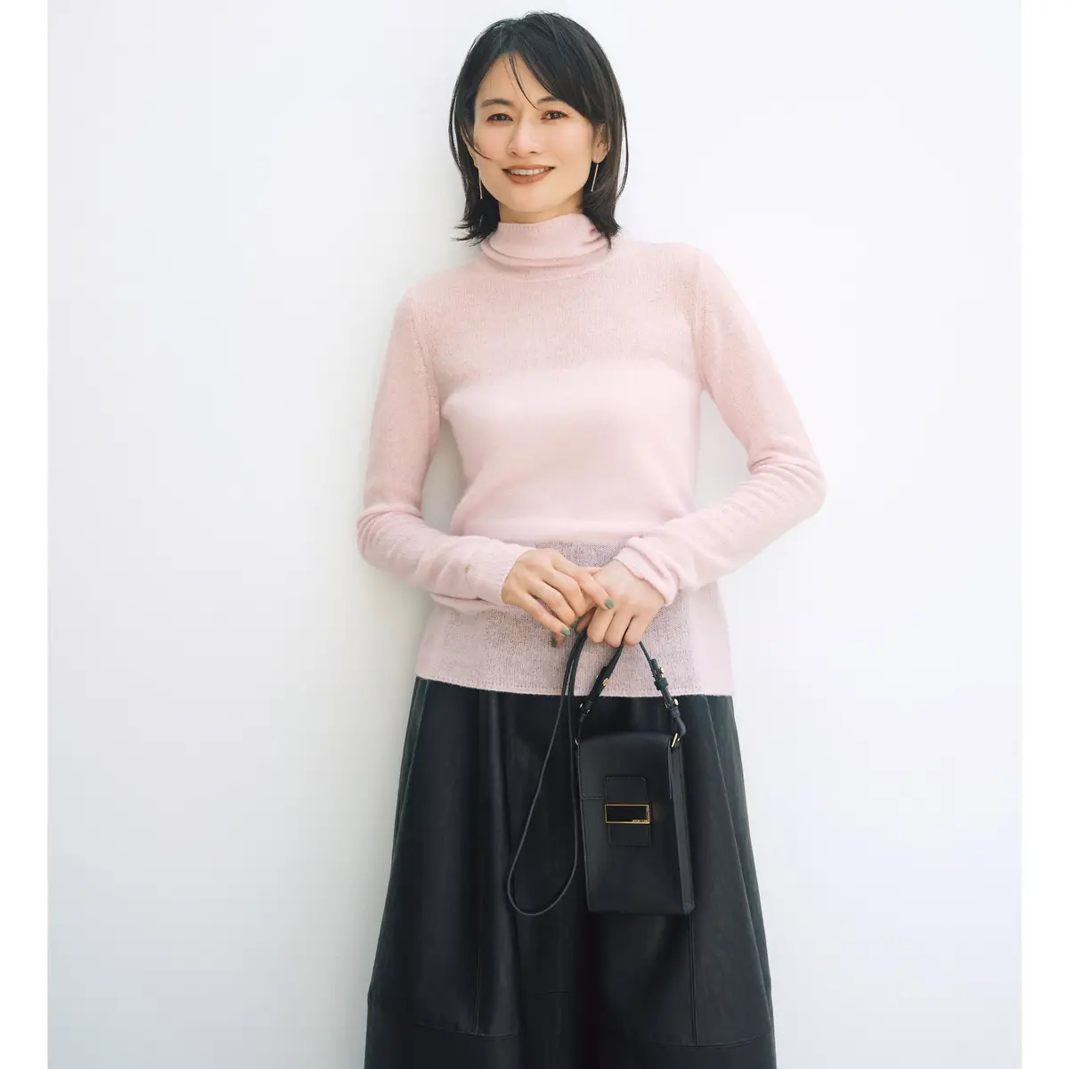 ダークグレーのタートルネックニットに、濃いめのワイドデニムを合わせた女性全身像。黒いショルダーバッグを持ち、シルバーのパンプスを履いている。背景はベージュと白の壁。