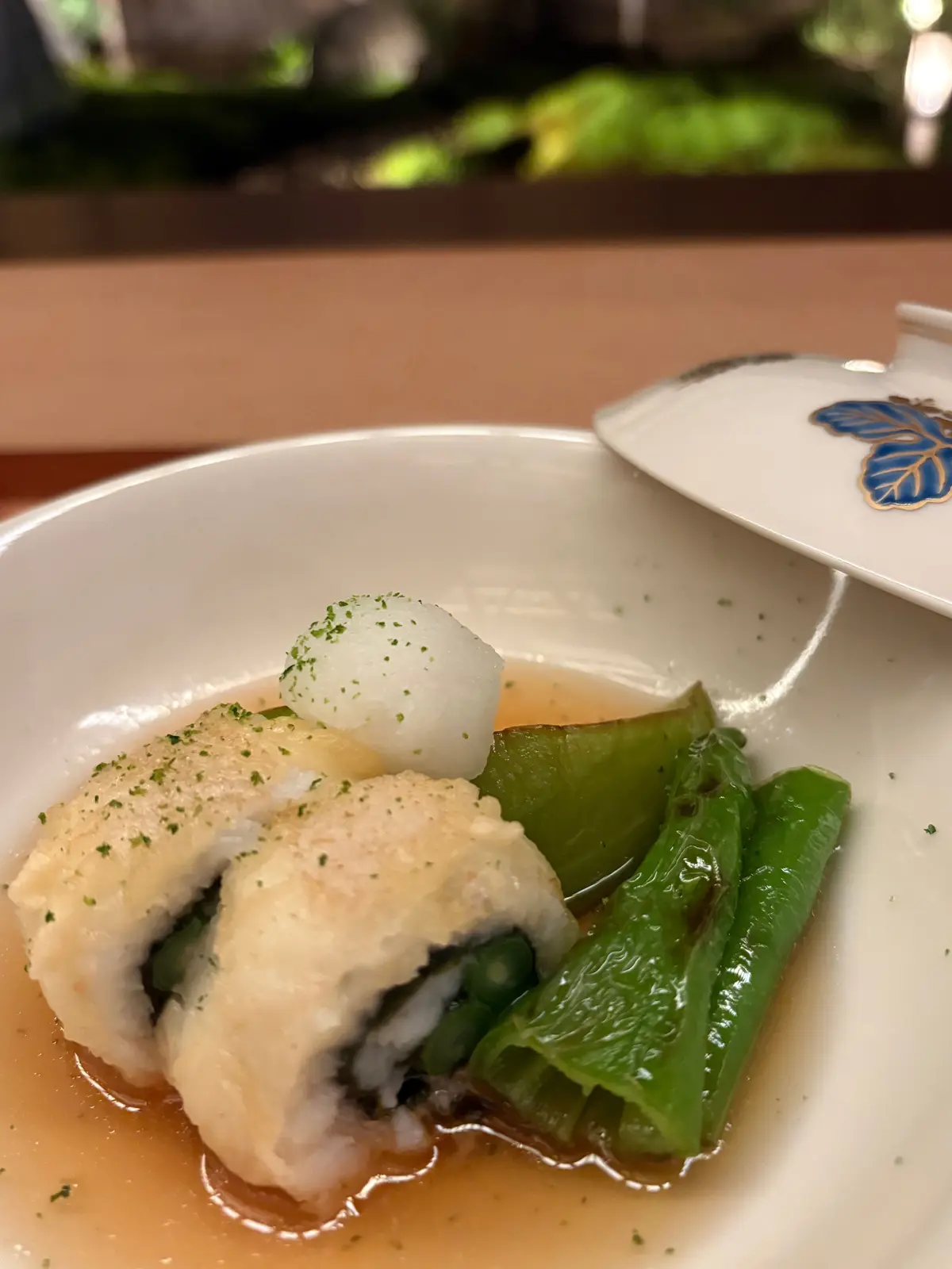 白磁皿に盛り付けられた、和食の料理。茶色い照り焼きソースをかけた豆腐の上に、細かく刻んだネギが散らされ、その上に白いお餅が置かれている。右隣には、茹でた緑色の青梗菜が添えられている。