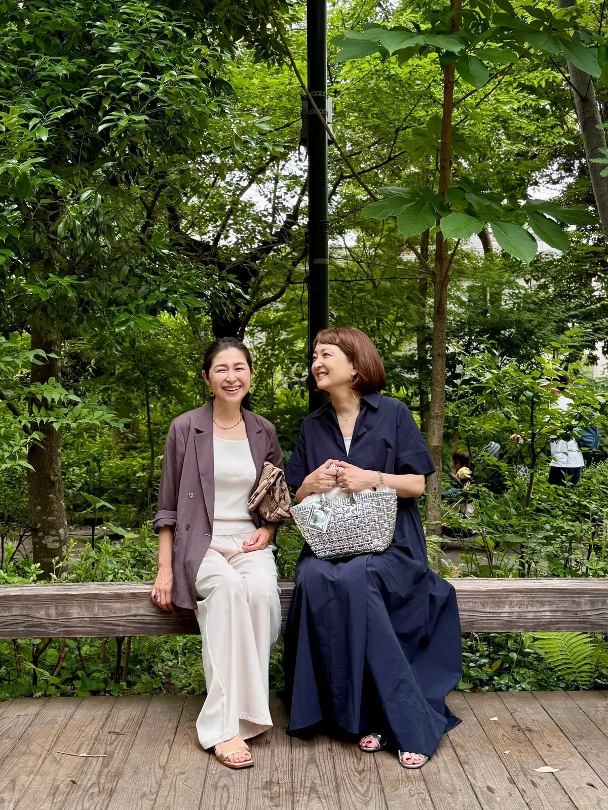 木製ベンチに座る二人の女性、緑豊かな庭園の背景