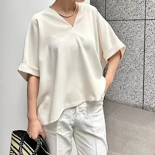 白くゆったりとしたシルク素材のVネックシャツ。短めの袖で、裾は少し後ろに長くなっている。白いパンツと合わせて、都会的なシンプルなコーディネート。