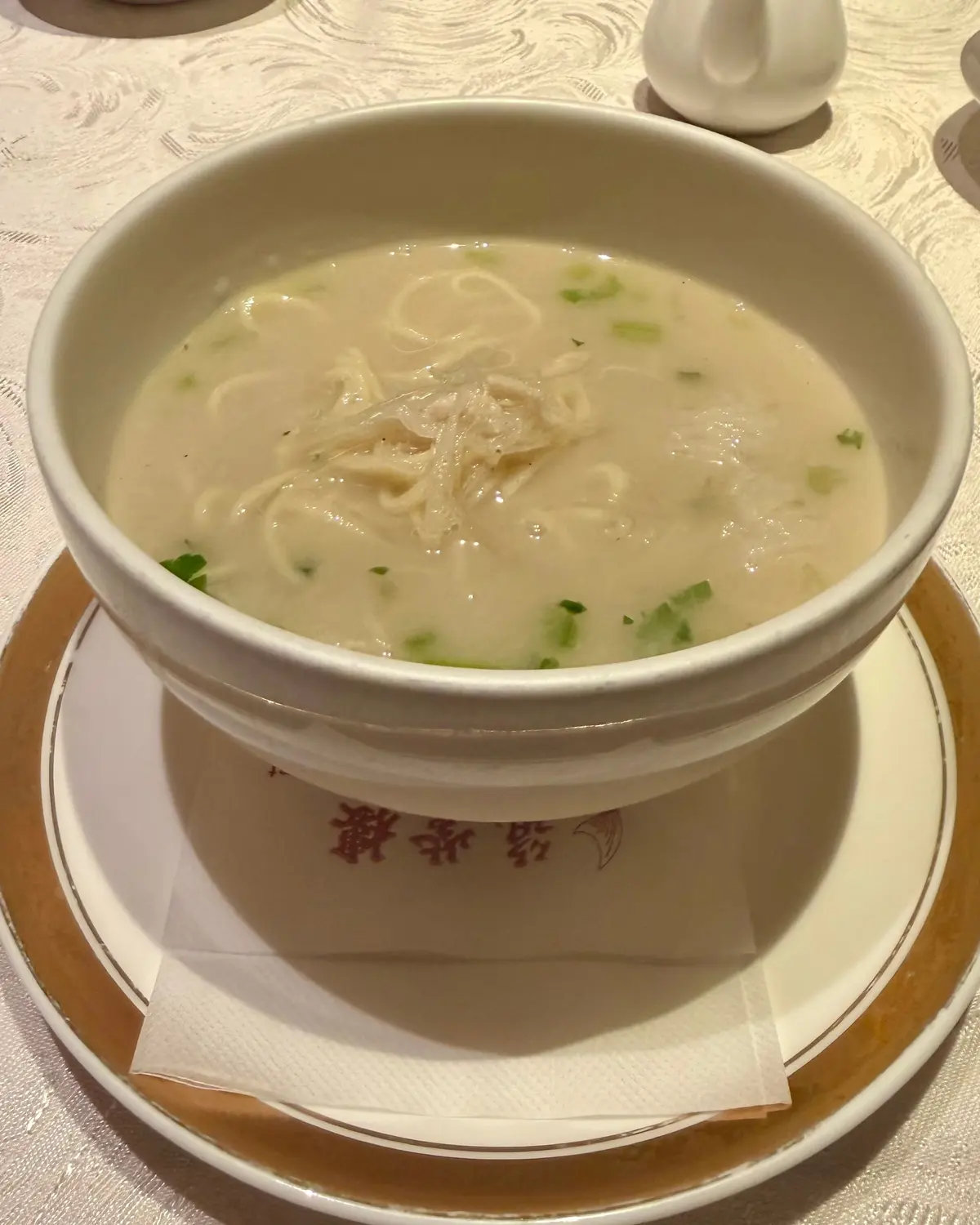 白いボウルに、細麺と緑のネギが散りばめられた淡いスープが盛り付けてある