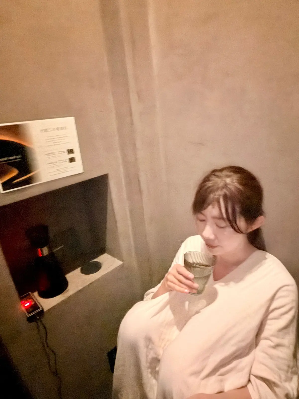浴衣姿の女性が部屋でグラスを手にしています。壁には案内パンフレットが貼られ、左側に小さなテーブルに香り器が置かれています。