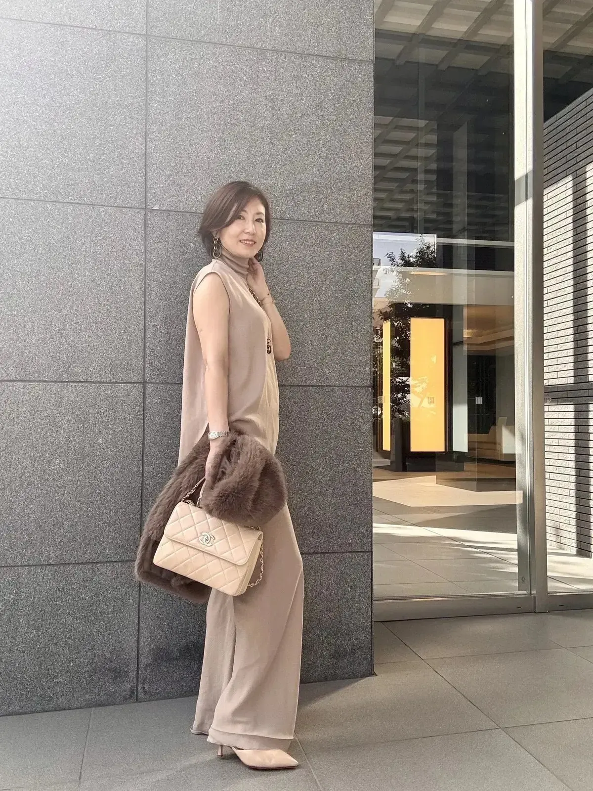 ベージュのセットアップを着た女性。右手にシャネルのバッグを持つ。ブラデリスニューヨークのブラタンクトップをインナーに着ていて、きれいなサイドシルエット。
