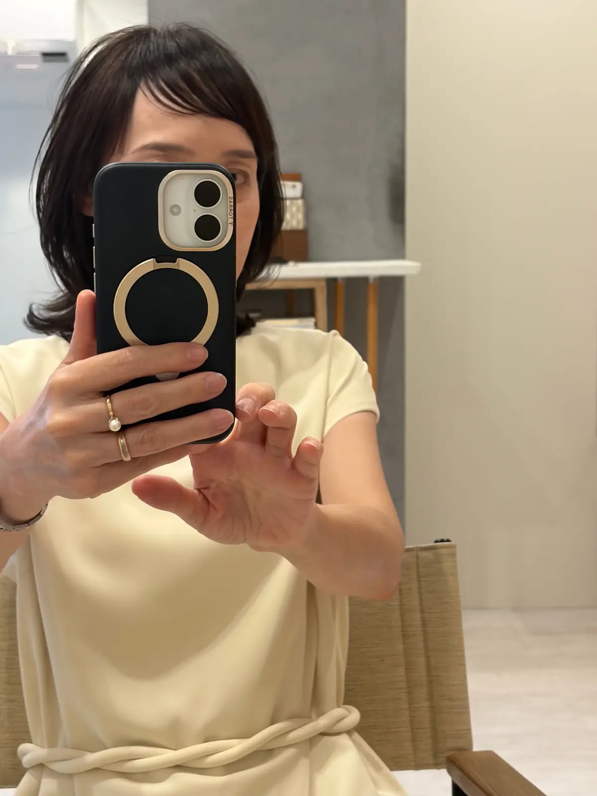 ベージュのトップスを着た女性がスマートフォンで自撮りをしている。