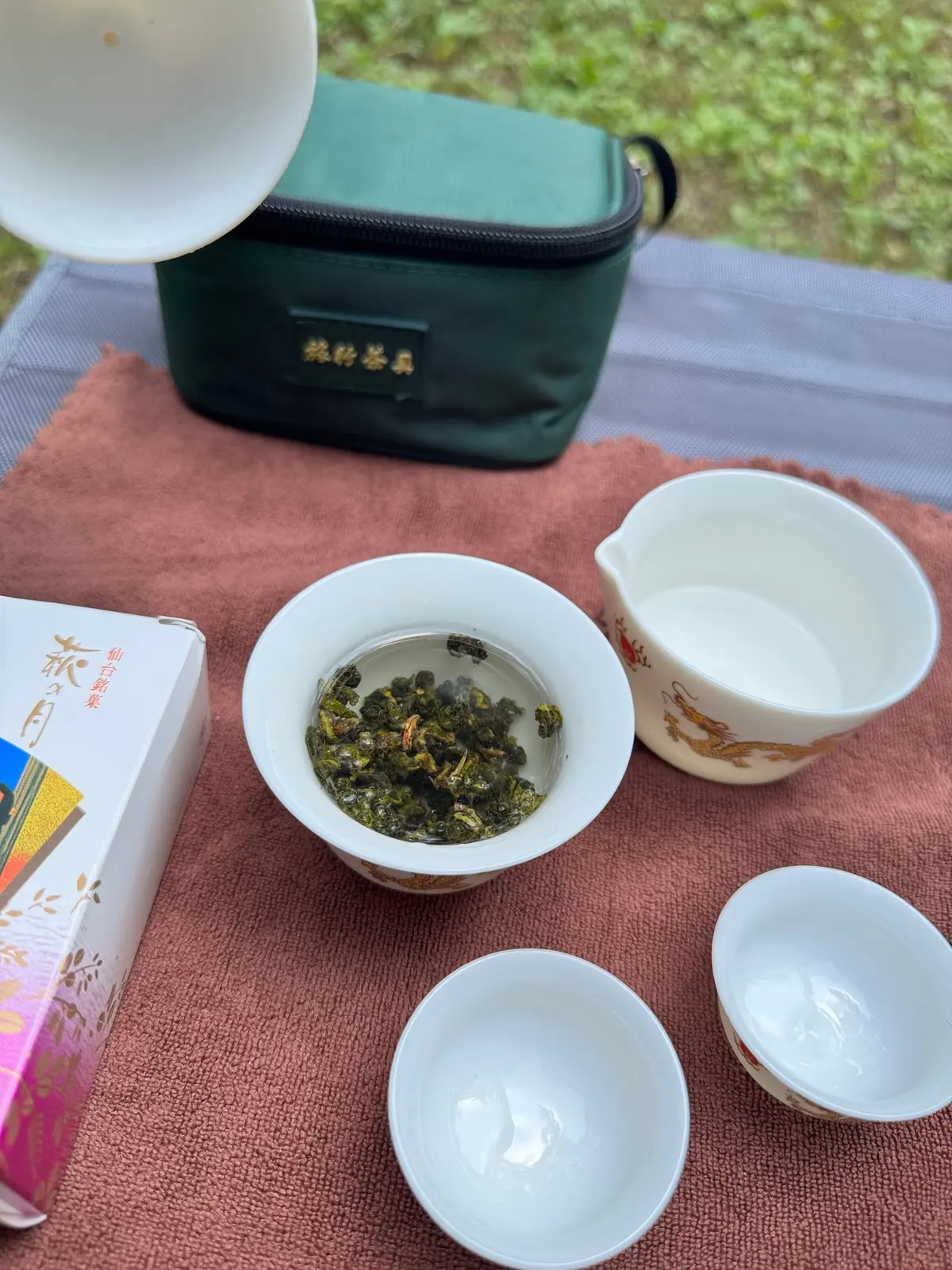 茶葉を淹れた白磁の茶碗と、茶碗を置いた緑色の茶筒、そして空の茶碗が置かれた様子。背景には赤茶色のマットが敷かれている。