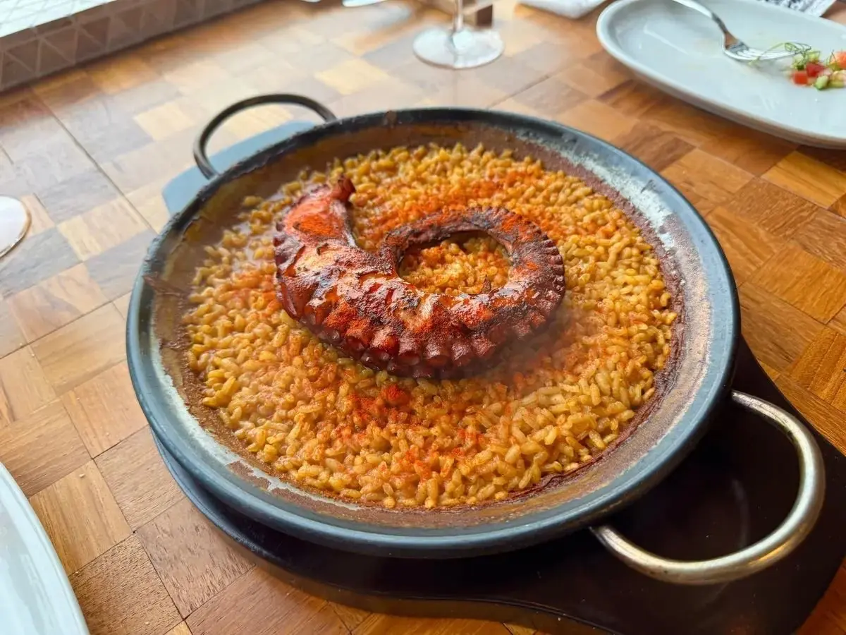 黒いパエリア鍋に盛り付けられた、オレンジ色のパエリアと、中央に大きなイカが乗った料理。イカは赤茶色で、触手が幾重にも重なっている。