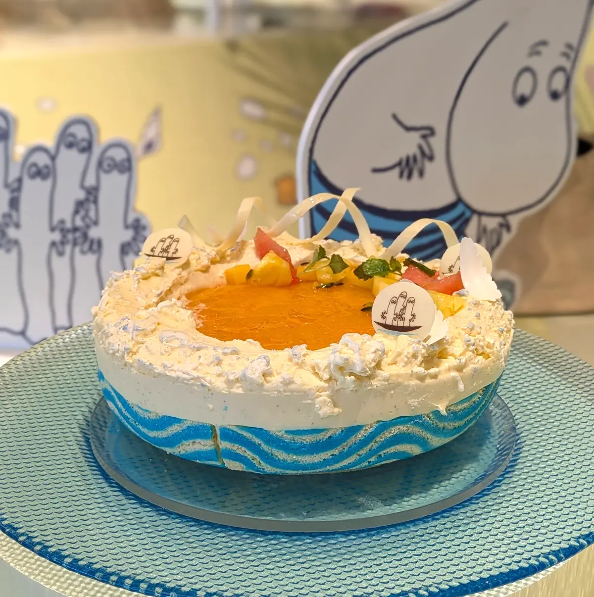 丸いケーキが青いプレートにのり、オレンジのゼリーとフルーツ、クリームで飾られている