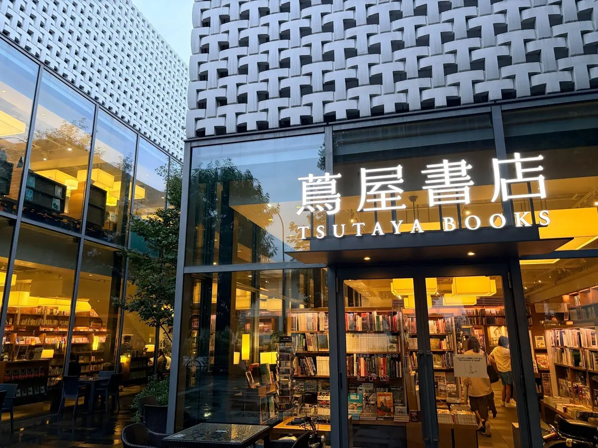 代官山蔦屋書店。ツタヤBOOKSの店舗外観。ガラス張りの建物で、店内には本が並んでいる。右側の壁面は幾何学模様の白い装飾。看板には日本語と英語で店名が表記されている。