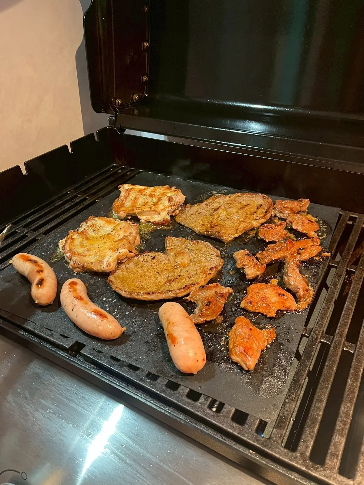 オーブンの天板に、鶏肉、豚肉、ソーセージが並んで焼かれている。鶏肉は黄金色に、豚肉は赤茶色、ソーセージはピンク色。
