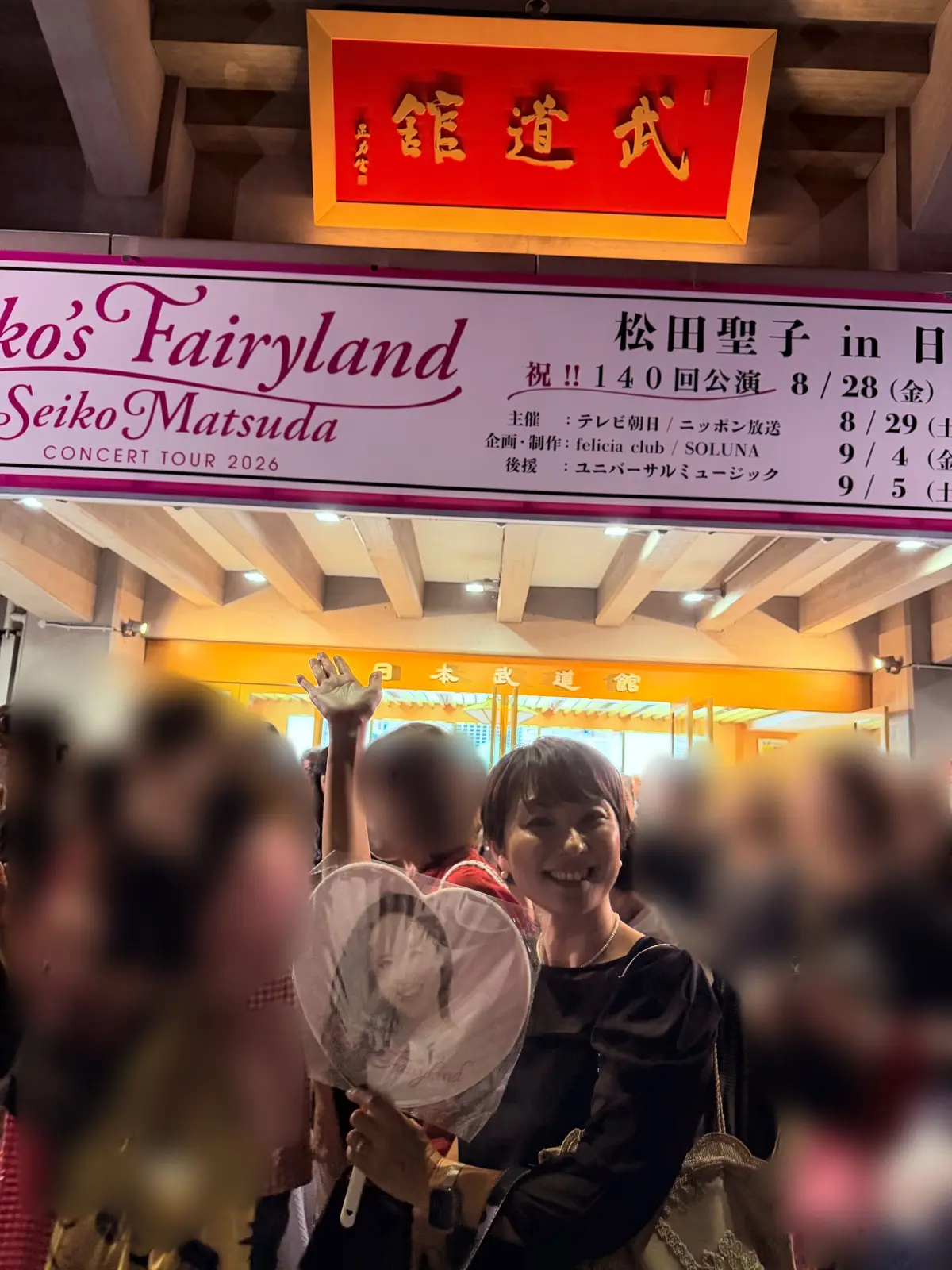 松田聖子コンサート「Seiko's Fairyland」の会場入り。女性が笑顔で白い犬を抱き、背景に会場の看板が見える。