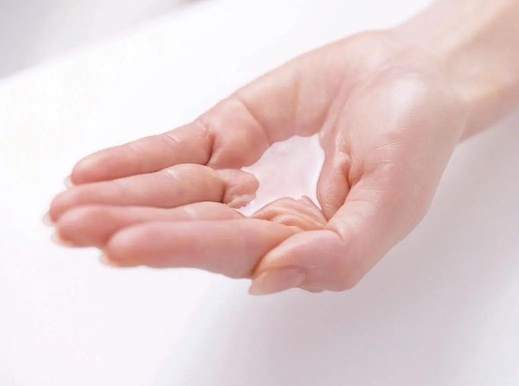 白い背景に、女性の手のひらに透明な液体が乗っている。液体は薄く広がり、手のひらの形に沿っている。