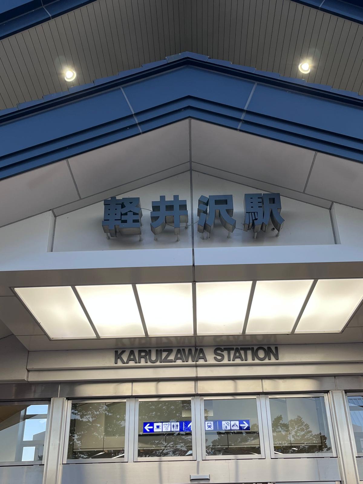 軽井沢駅の駅名標。上部に日本語の「軽井沢駅」の看板、中央に英語の「KARUIZAWA STATION」の表示がある。駅舎の入り口はガラス張りの構造になっている。