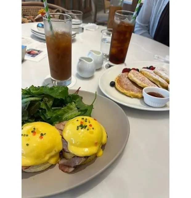 テーブルに置かれた朝食の盛り合わせ。左にはエッグベネディクト、右にはパンケーキ。それぞれに飲み物（アイスティー）とミルクピッチャーが添えられている。
