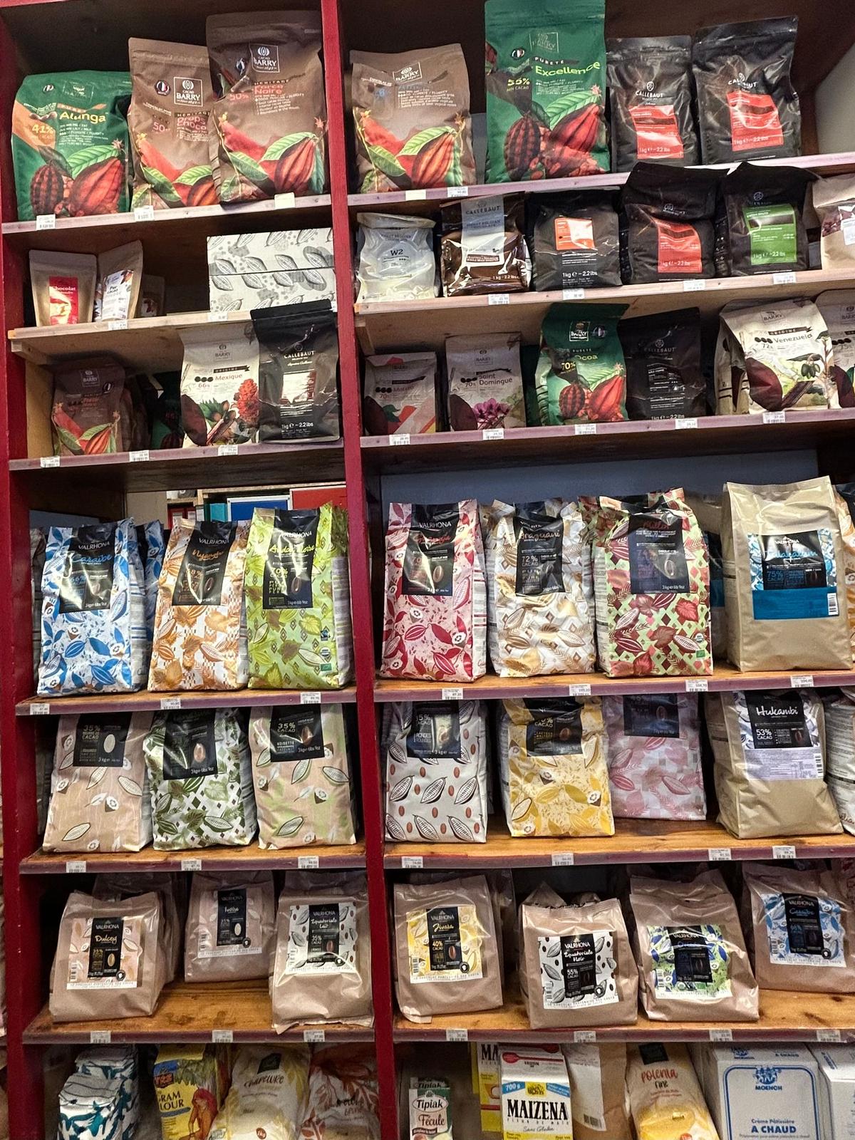 赤色の棚に、様々な種類のチョコレートや粉末状の食品が並んでいる。各商品は茶色や緑色、ピンク色などの包装紙で包まれ、棚の上部にはバレンタインの装飾品が置かれている。