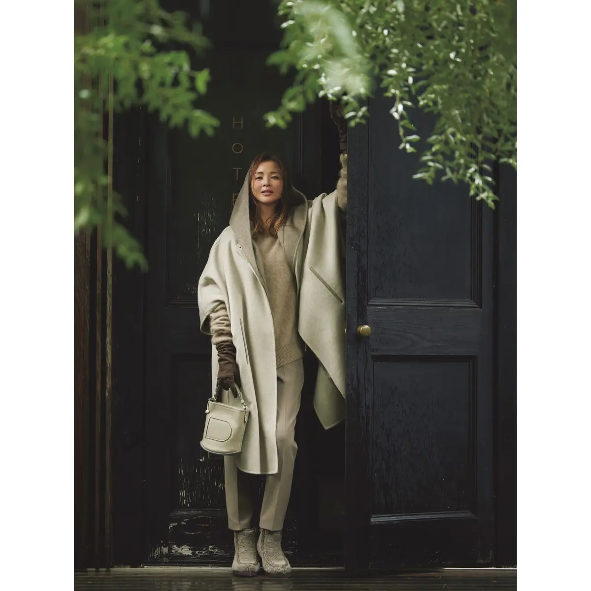 ベージュのマントコートにフードつきストールを重ね着し、ベージュニットとパンツを合わせたワントーンのコーディネート　モデル・SHIHO　