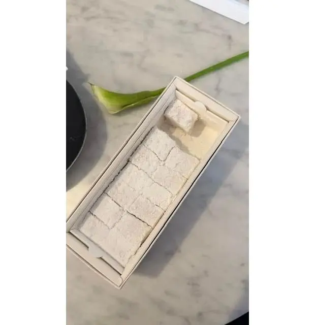 長方形の木製トレイに整列した白い和菓子と、緑の葉が添えられた花