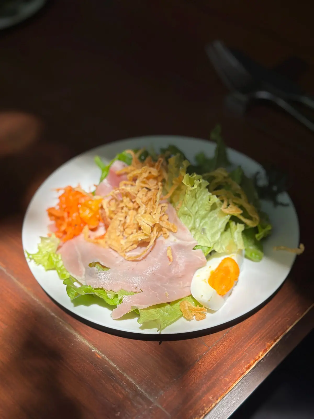 白い皿にレタス、ハム、カラフルな野菜、ゆで卵、トーストしたパンのスライスが盛り付けられたサラダ
