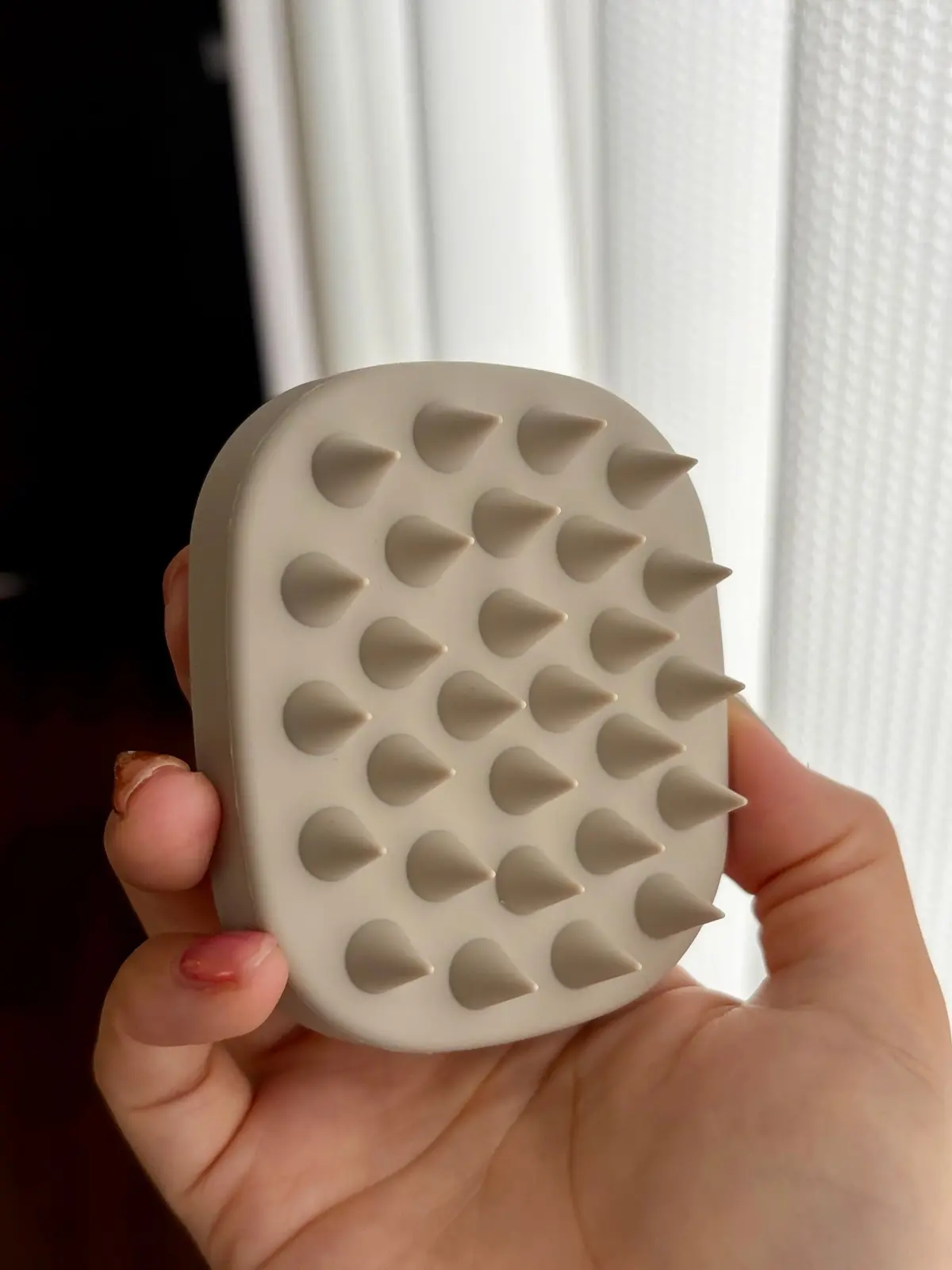 ベージュ色のシリコン製の、多数の突起がついたマッサージツール。手で保持されており、突起が上を向いている。