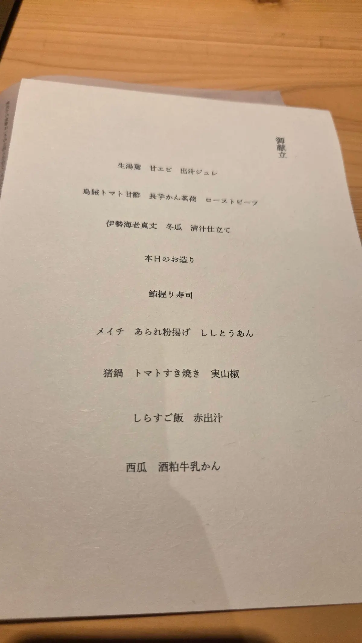 白紙に黒色の文字で書かれた日本のレストランのコース料理メニュー。上部に「御膳立」の文字、その下に料理名が縦書きで列挙されている。