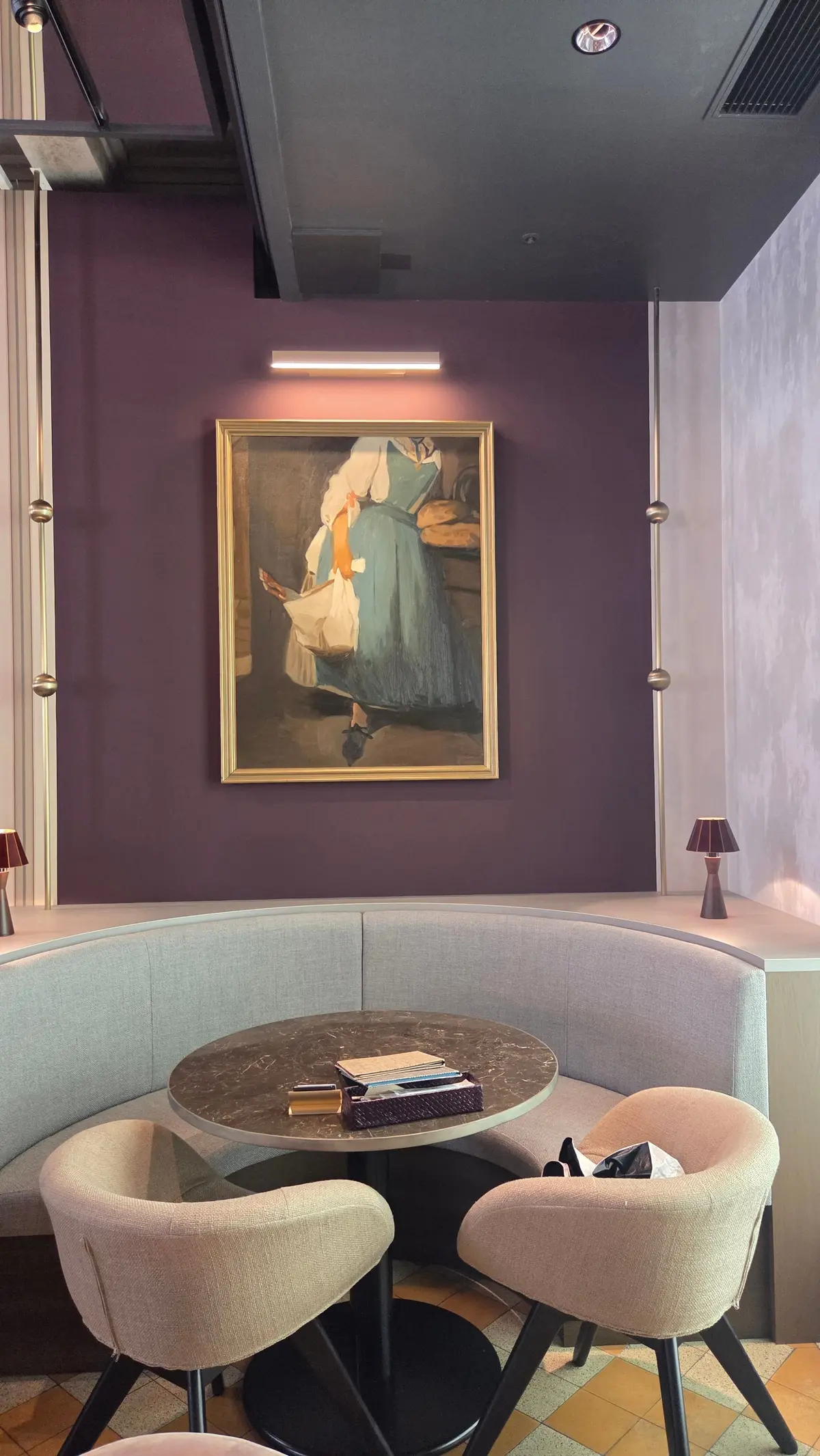 紫色の壁に額装された絵画があり、丸いテーブルとベージュの椅子が配置されたモダンな内装の空間。