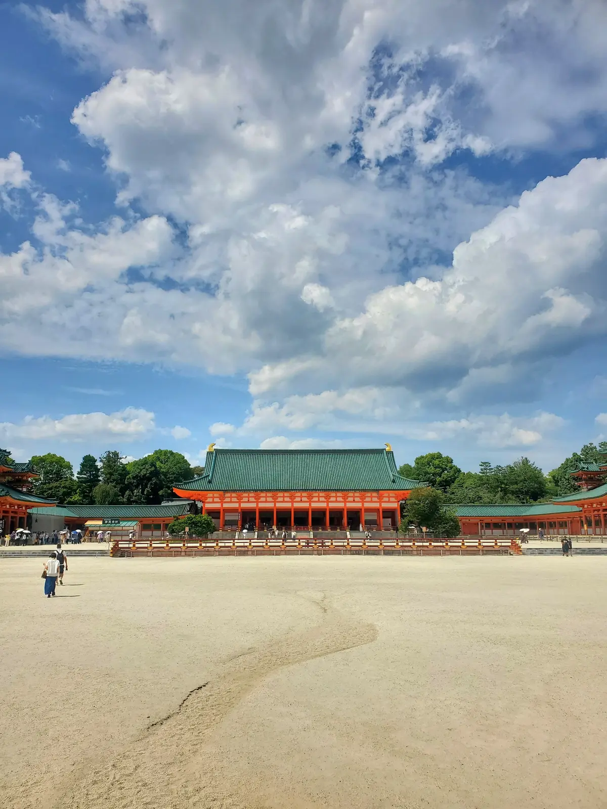 広大な砂地に、朱色の柱と緑色の屋根の伝統的な日本の建物が並ぶ。青空に白い雲が広がり、晴れた日の風景。