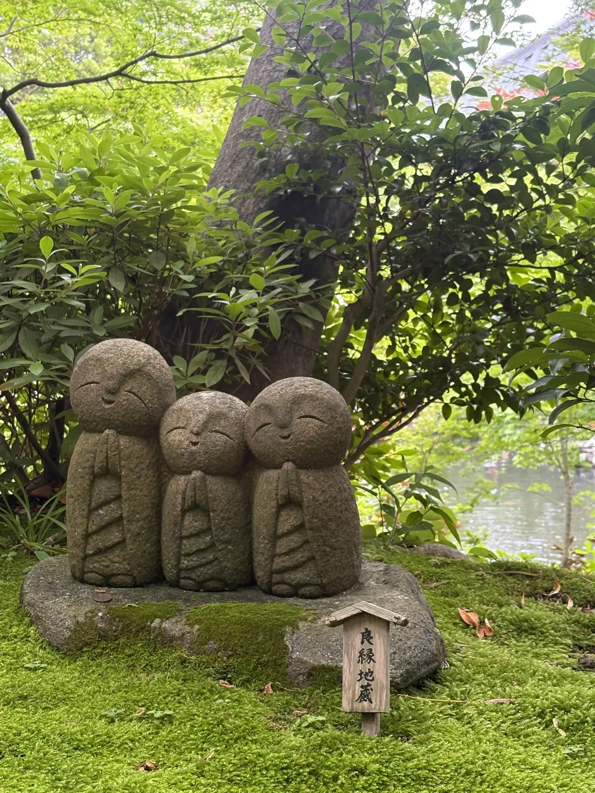 石の仏像3体が並ぶ庭、苔むした岩と木々が背景
