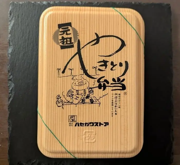長方形の食品容器。表面には「ハセガワストア」のロゴと、手書き風の文字、イラストが描かれている。