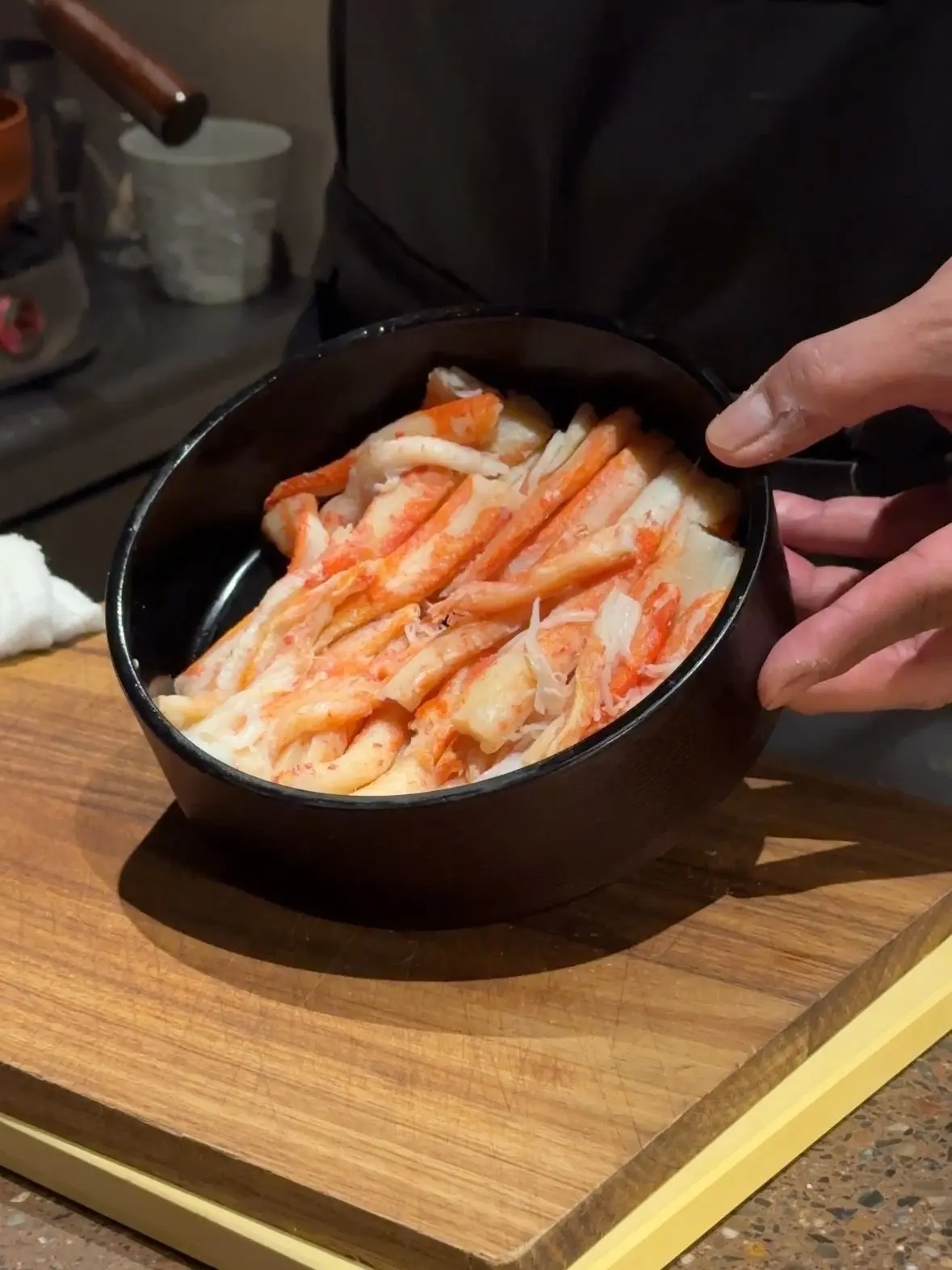 厨房で作業する男性と、カウンターに並べられた料理やグラス。銅製のカップ、木製のトレイ、水差しなどが置かれている。