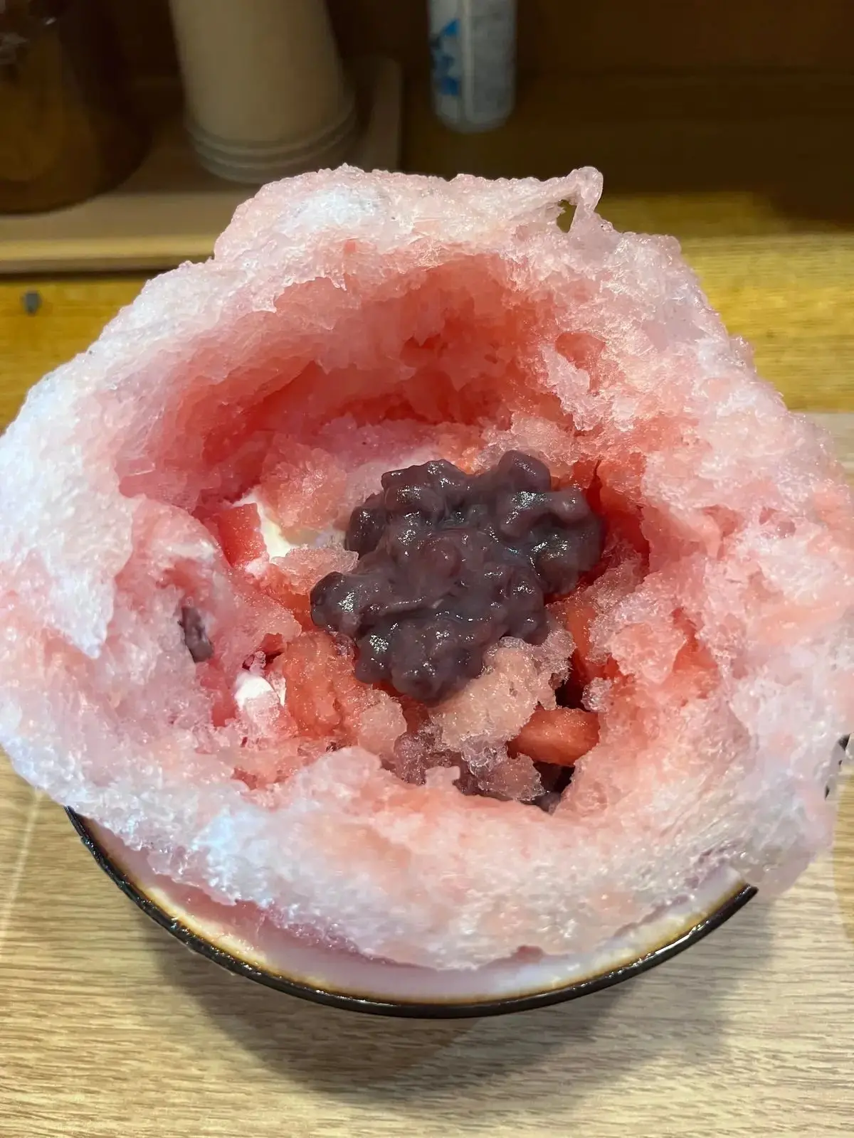 黒蜜とあずきが乗った、ピンク色のかき氷。器に盛り付けられ、雪のようにふわふわとした食感に見える。