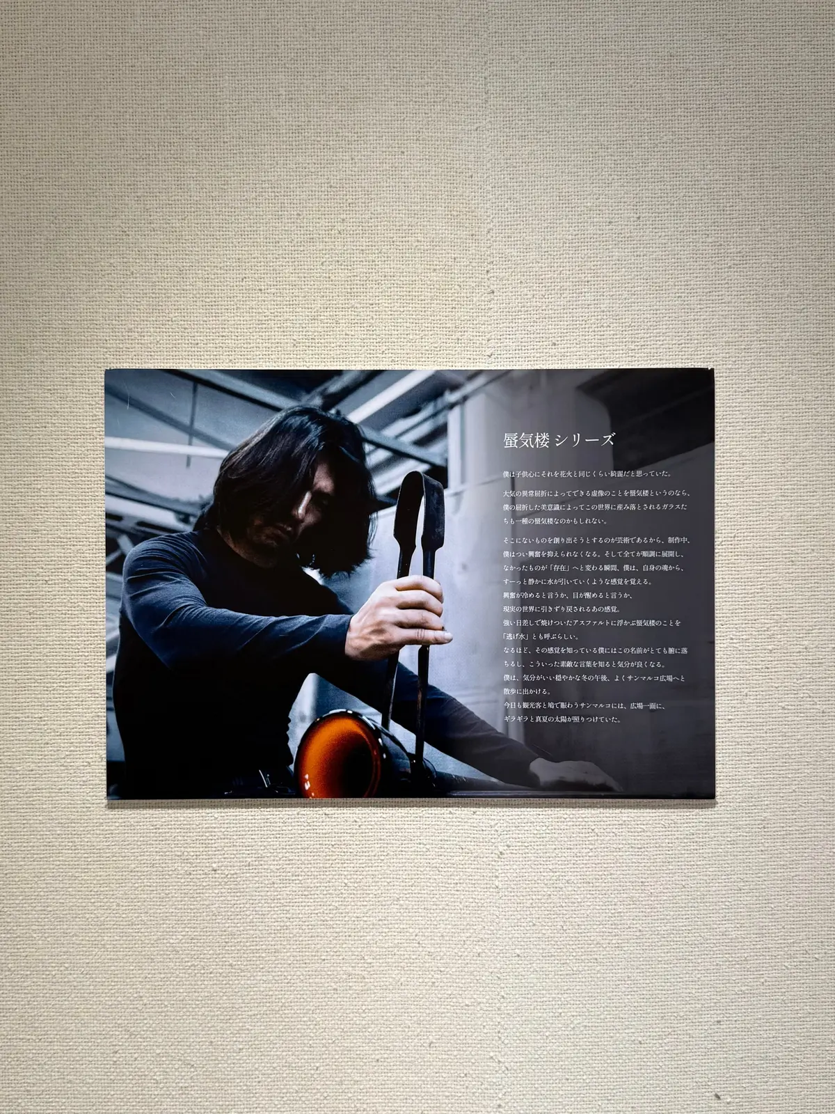 左下に男性がハサミを持ち、右側に男性がミシンを使用している工房の様子。背景には裁縫道具や生地が置かれ、右ページには日本語のテキストが印刷されている。温かみのある色調で、手仕事の温もりを感じさせる。ヴェネツィアンガラス作家の土田さんの工房。ヴェネツィアのムラーノ島。